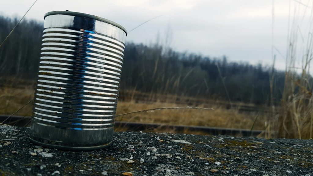 Tin can resting on a gravel surface near rural railroad tracks under cloudy skies.